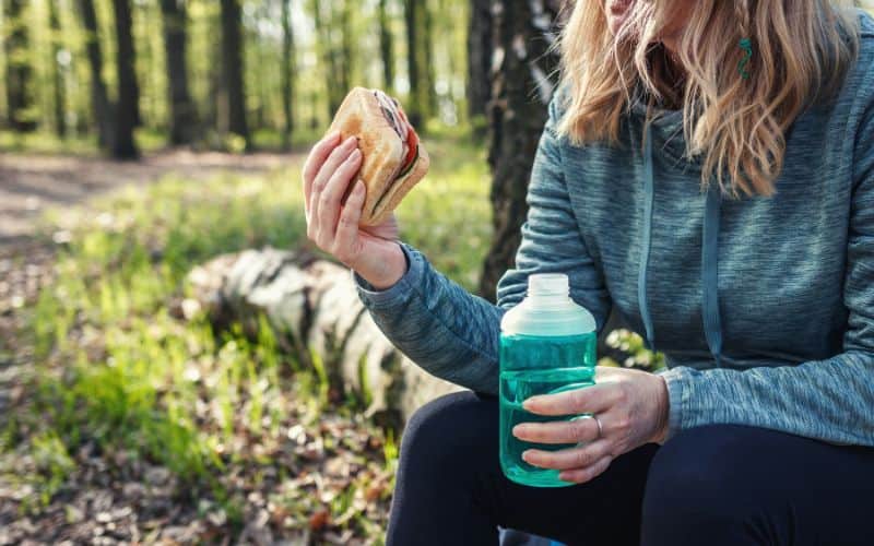 Camper eating sandwich and holding a bottle of water 