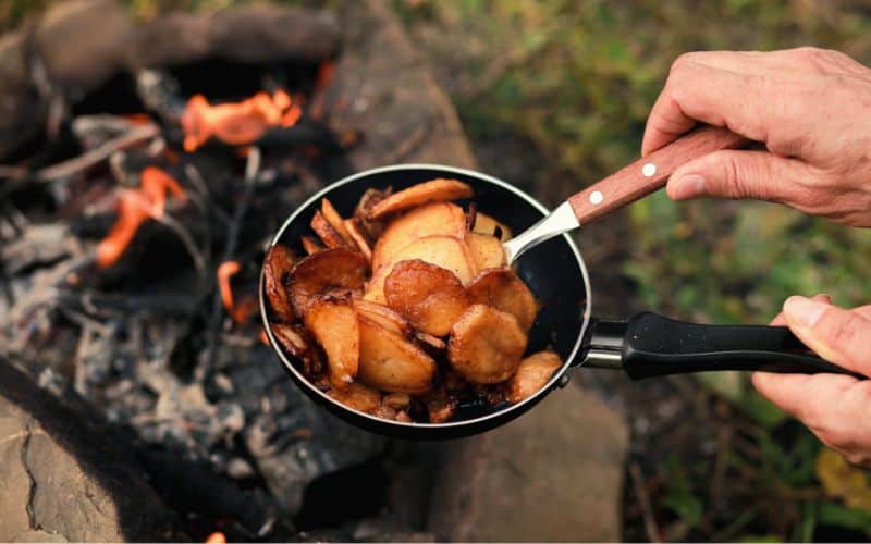 Campfire Potatoes and Sausage in pan front of campfire 