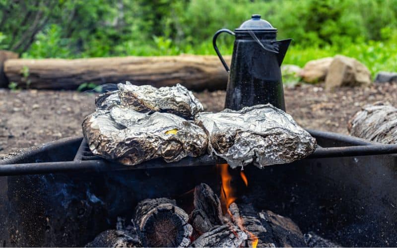 Foil wrapped food sitting on grate over a campfire