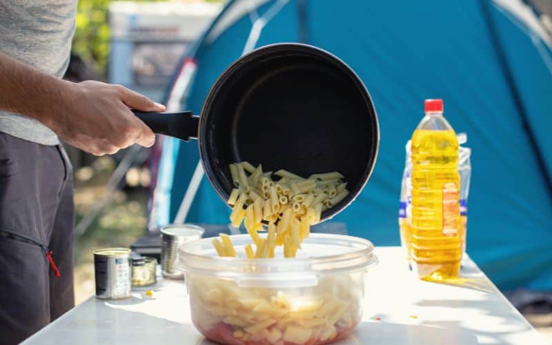 Man in front of tent pouring boiled pasta into container