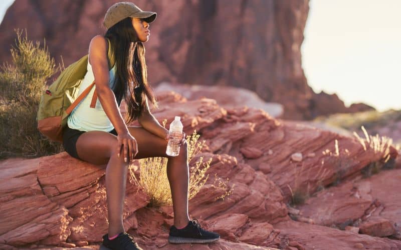 Woman hiker sitting on rock drinking water
