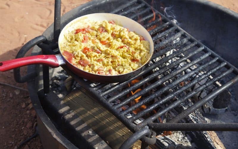 Scrambled eggs cooking a in a frying pan on a grate over a fire