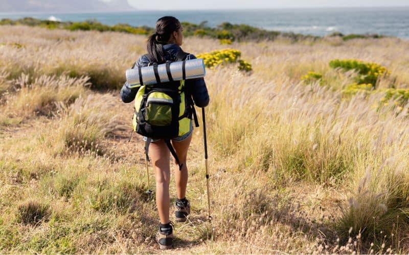 Woman backpacker walking through grass next to the coastline