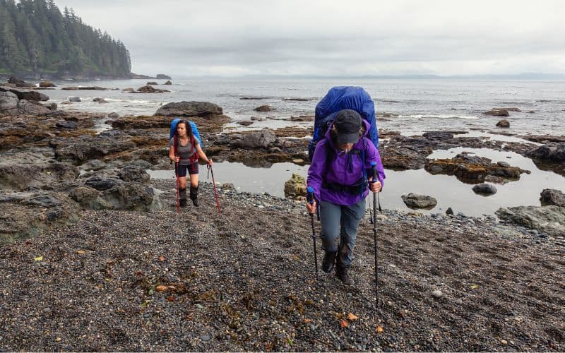 Women backpacking carrying trekking poles over rocky coastline