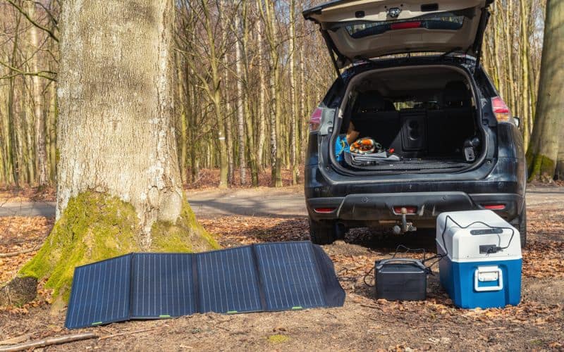 Electric ccamping cooler plugged into solar panel outside of car trunk