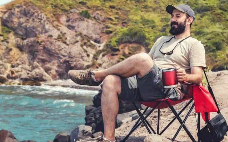 Tall man sitting in camping chair beside the sea